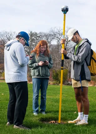 Three students set up a telescopic pole on green grass