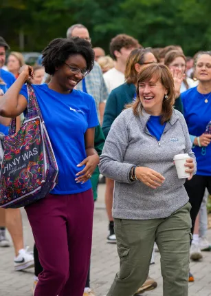 Two U N E employees walking and laughing amongst a group of other employees on campus