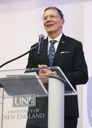 UNE President James Herbert smiles while speaking at a podium during the President's Forum event at the Harold Alfond Forum