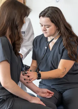 A U N E Physician Assistant student uses a stethoscope to check a classmate's blood pressure during a hands-on skills exercise.