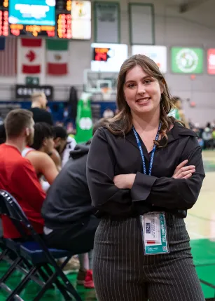 A U N E student wearing a lanyard smiles courtside during her internship with the Maine Celtics.