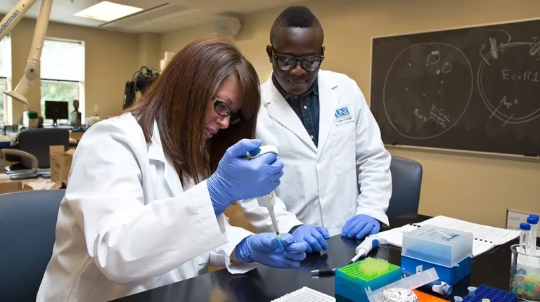 two students in lab coast and gloves work in a pharmacy lab
