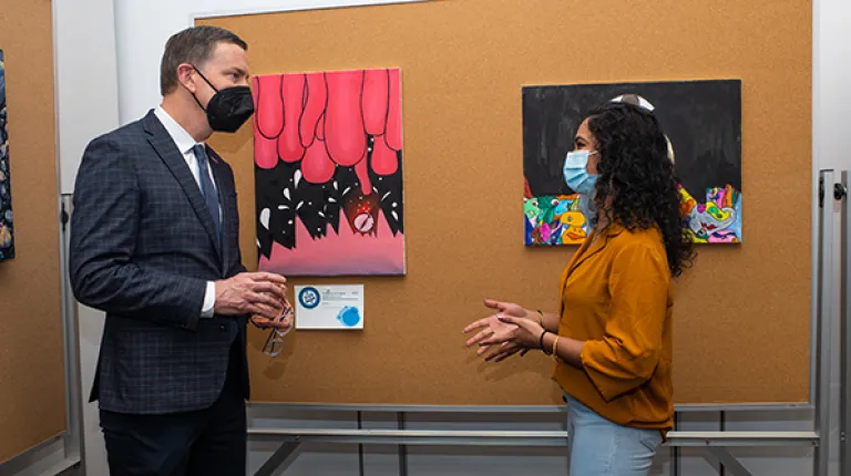 UNE President James Herbert talks with a student in front of her artwork at ArtCOM