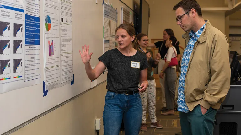 A poster presenter describing their research to an individual