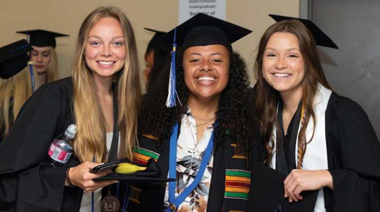 Three U N E students pose after graduation