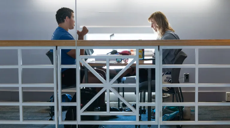 Two students talk while sitting in the Portland Campus library
