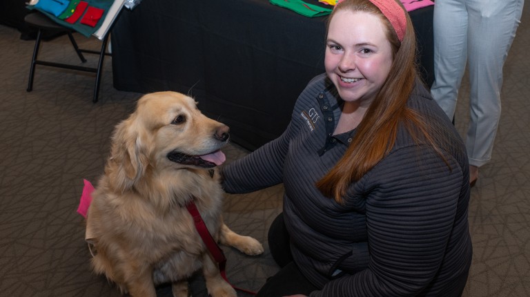 A pediatric center representative poses with a therapy dog, a Golden Retriever