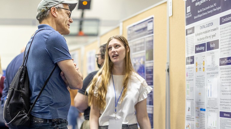 A student explains their research poster to an audience