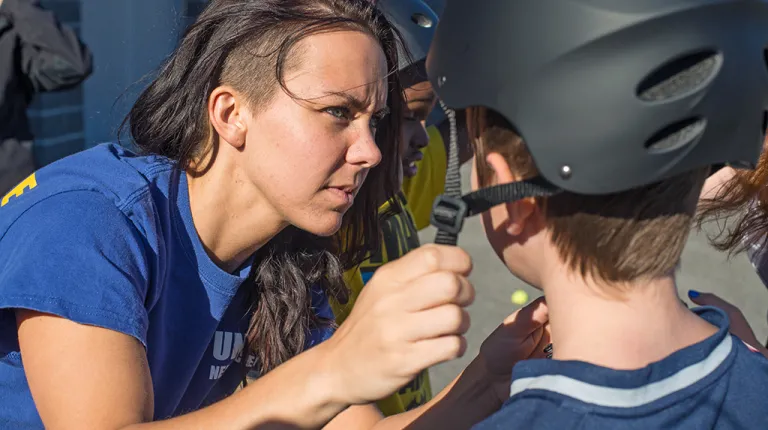 A student helps a child put a bike helmet on their head