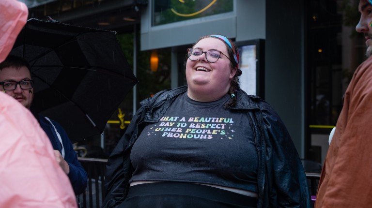 A woman's shirt reads "What a Beautiful Day to Respect Other People's Pronouns"