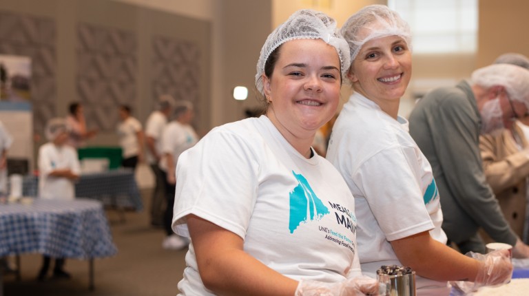 Two students pose for a photo while packing meals