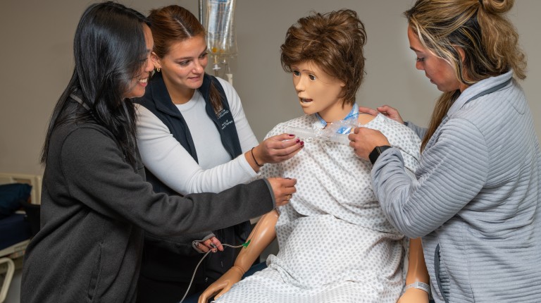 Three U N E students practicing on a patient simulator