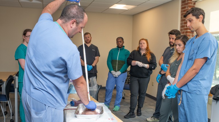 Physician Assistant students watch as their professor demonstrates stopping bleeding