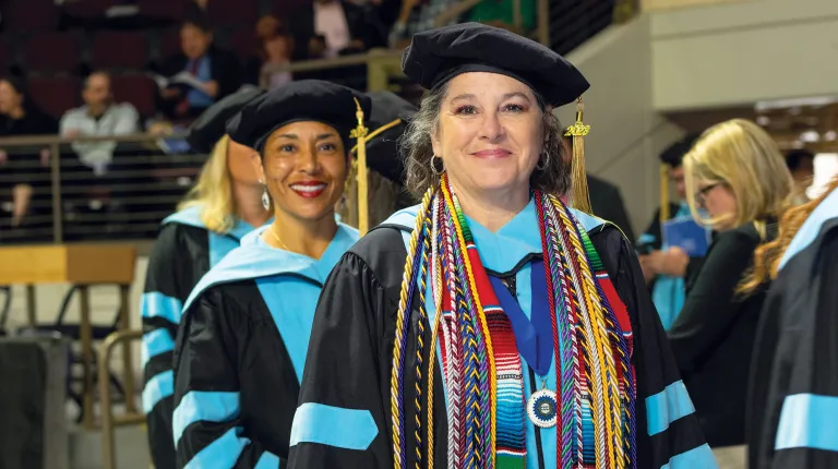 A graduating student smiles for the camera while waiting to cross the stage at commencement