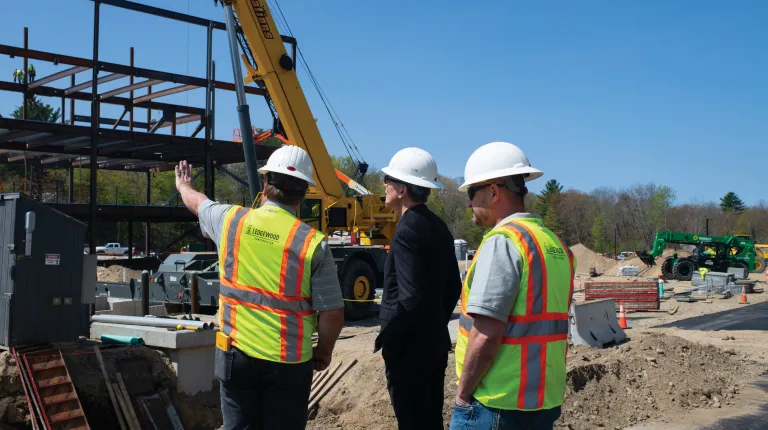 Three construction workers wearing hard hats examine the construction of the new U N E portland campus medical school building