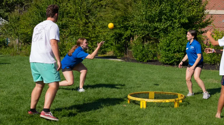 Three students playing a game with a ball and net on the Biddeford campus