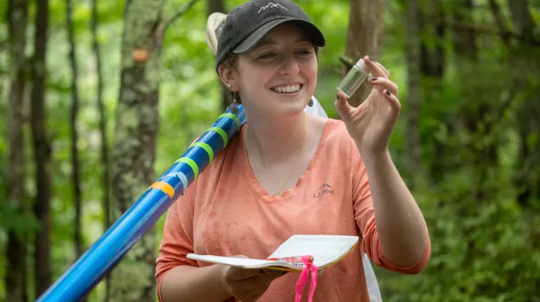 A student holds up a vial while doing research in a forest