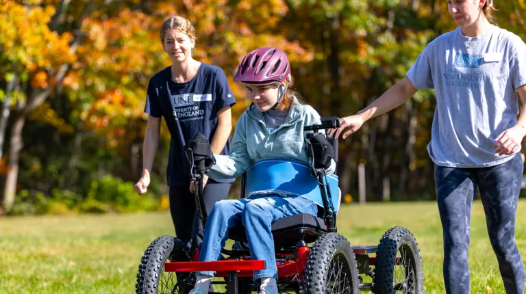 UNE volunteers assist a power soccer player outside