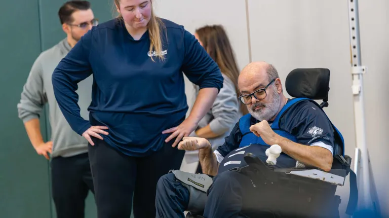 A UNE student assists a wheelchair user at the power soccer demo