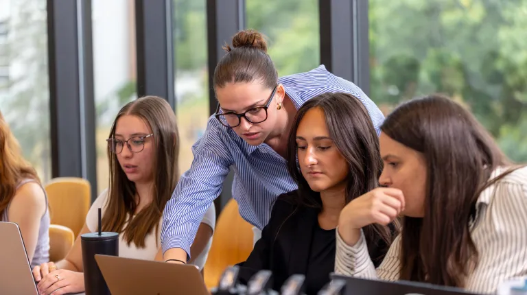 UNE students collaborate on a laptop around a conference table