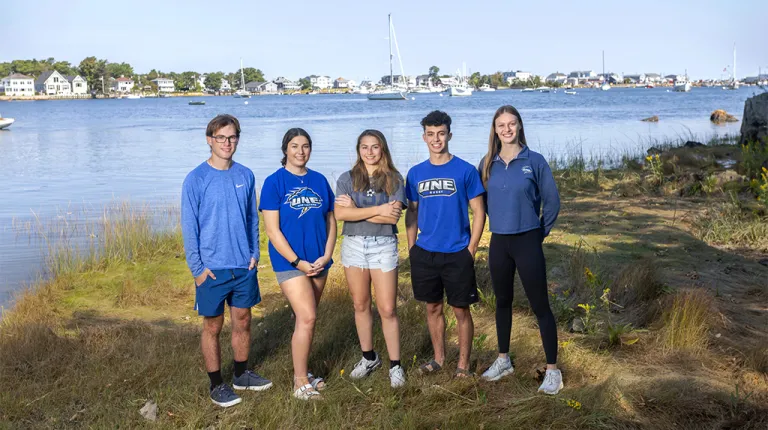 Five undergraduate UNE students stand in front of the Saco River