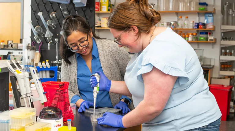Jennifer Garcia works with a UNE Student who pipets in the lab