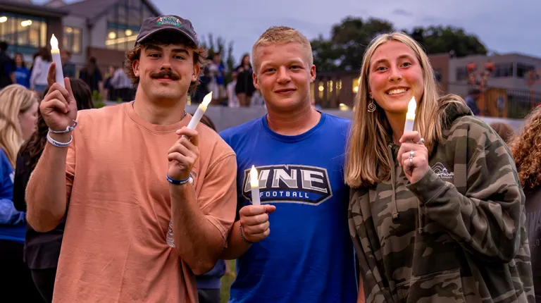 Three students hold up candles for the First Night event on the Biddeford Campus