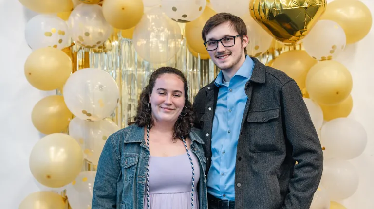 Two students pose for a photo in front of balloons