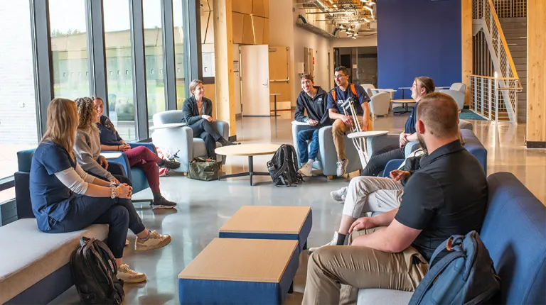 A large group of students sit with two professors in a lounge setting