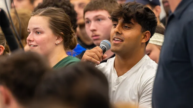 A student speaks into a microphone from an audience
