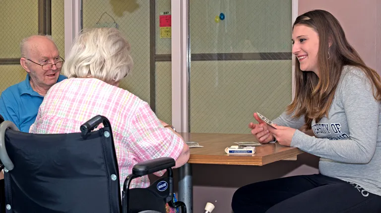 A student plays cards with two elderly residents at nursing home
