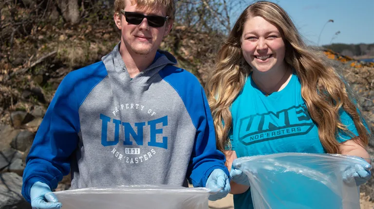 Two students hold up clear plastic bags as they participate in a beach clean-up event