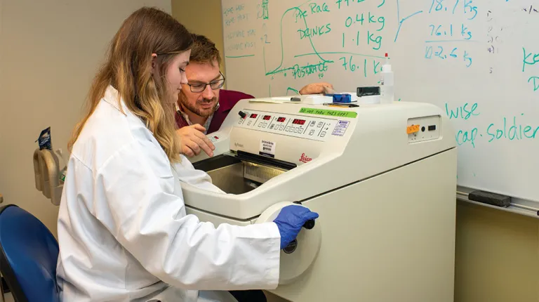 A student and their professor use a machine in a laboratory