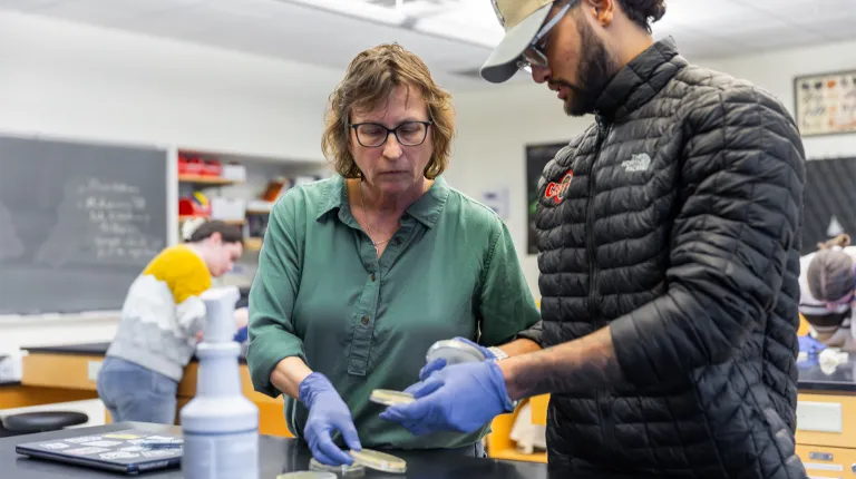 A biology professor assists a student with their petri dishes during a lab