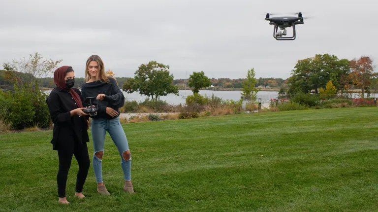 Two Shaw Innovation Fellows pilot a drone over the UNE waterfront campus during fieldwork for their fellowship project on an overcast autumn day