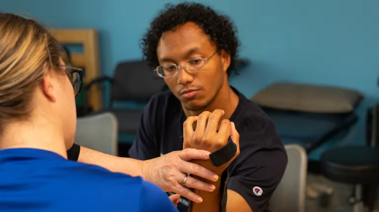 An occupational therapy student practices a wrist assessment technique on a classmate wearing a support brace.