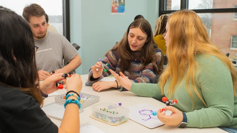 Four students work together around a table in the Student Academic Success Center, assembling molecular models and discussing chemistry concepts.