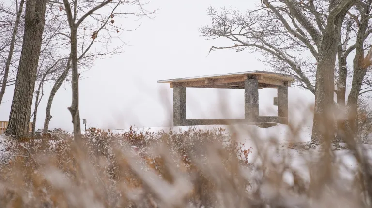 A stone-and-wood pavilion at Jordan's Point on U N E's campus, dusted with snow during a winter storm.