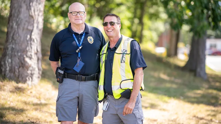 Two U N E security staff members smile together outdoors at the Fall Assembly event.