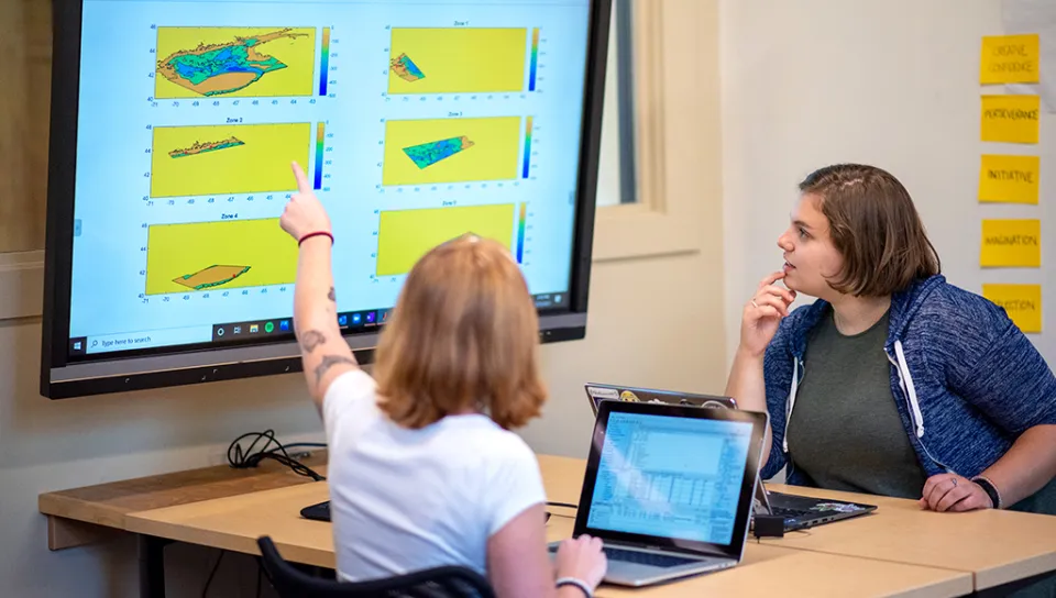 Two students study charts on a large screen