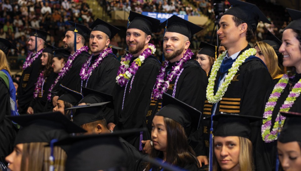Students sit wearing caps and gowns and leis during the 2022 commencement ceremony