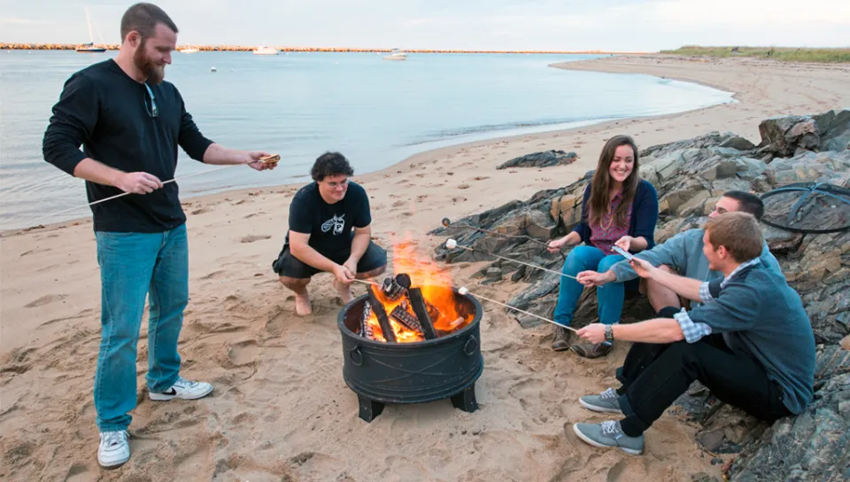 Several students sitting on the beach and having a bonfire