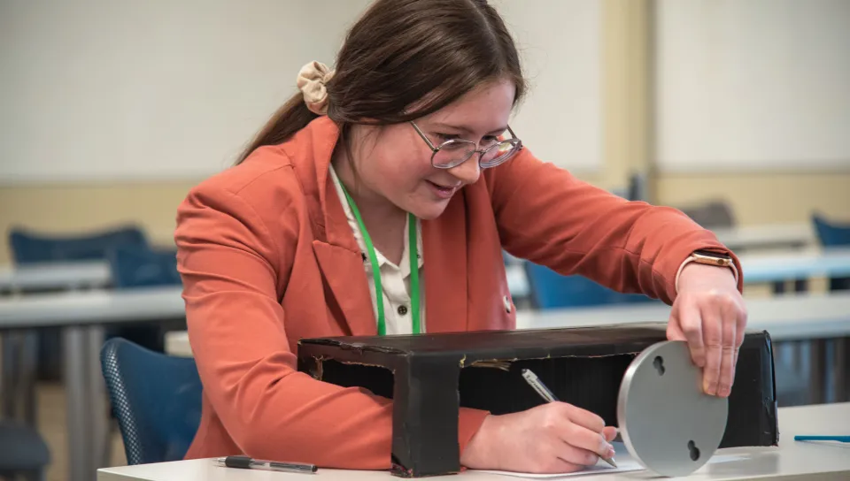 A female student uses a mirror to draw a shape using only oral instructions