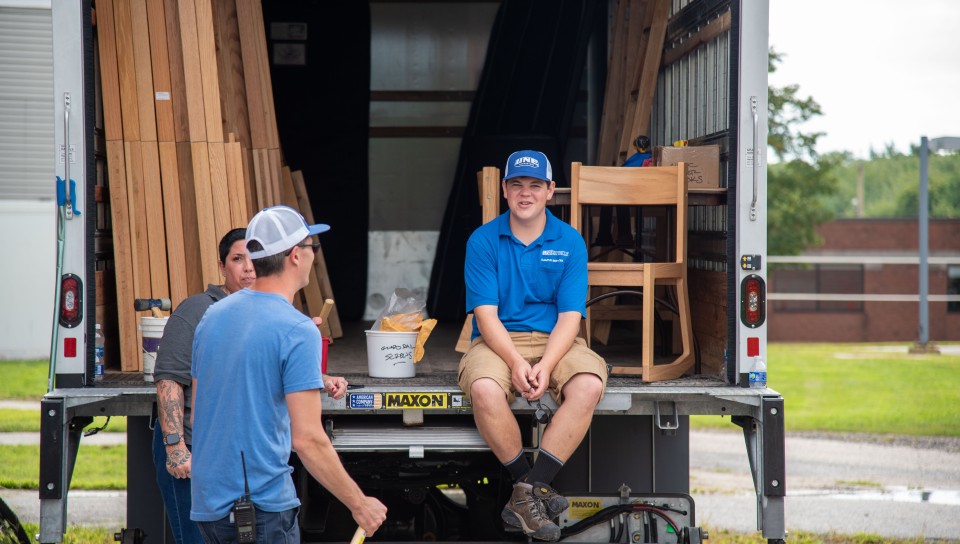 A student sits in a moving truck containing dorm furniture