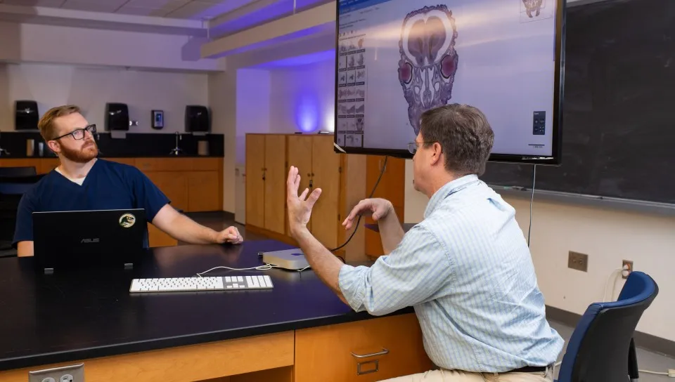 A professor speaks with a student in a classroom