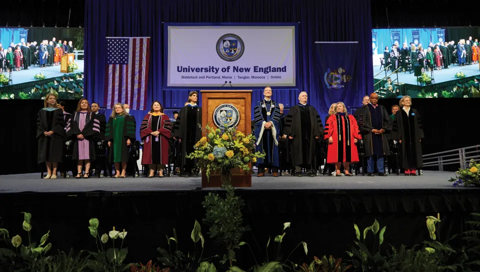 faculty stand on the stage at the U N E 2023 commencement ceremony