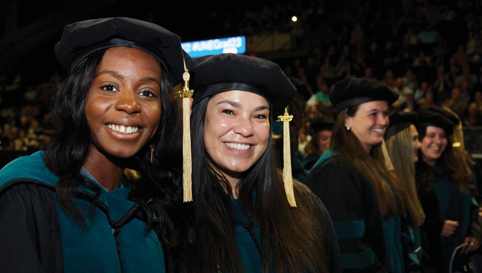 Two graduating students smile for the camera during the 2023 U N E commencement ceremony