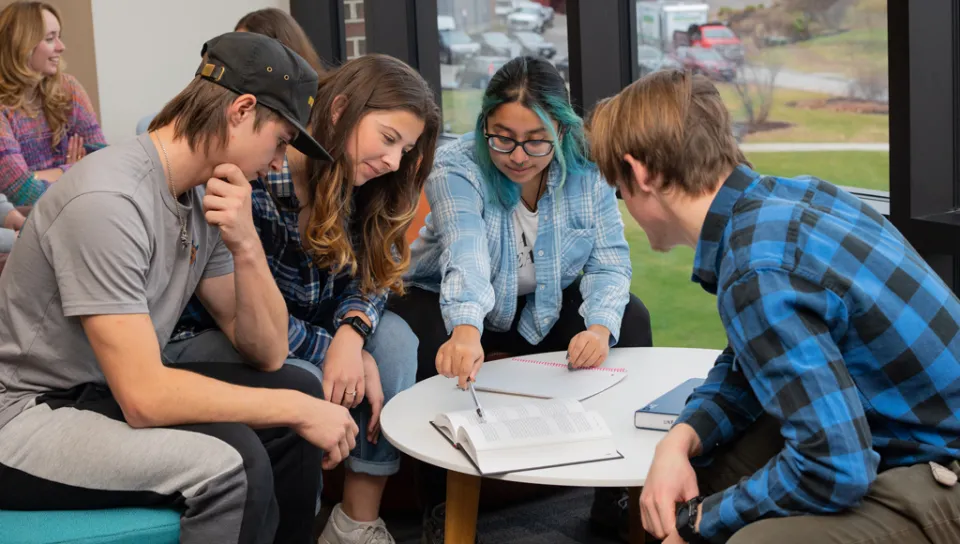A group of students sit over a table and study in the Commons
