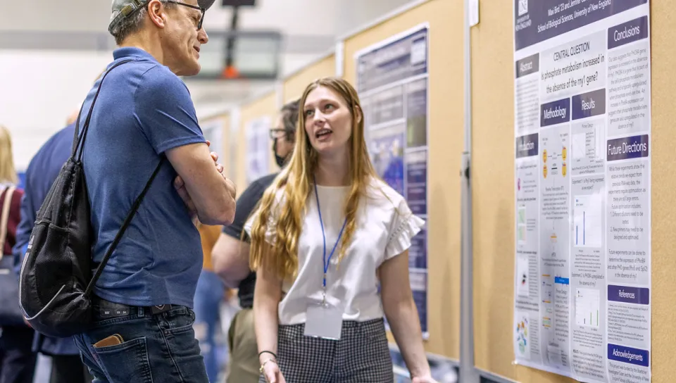 A student describes their research poster to an audience member at an Undergraduate Research Symposium