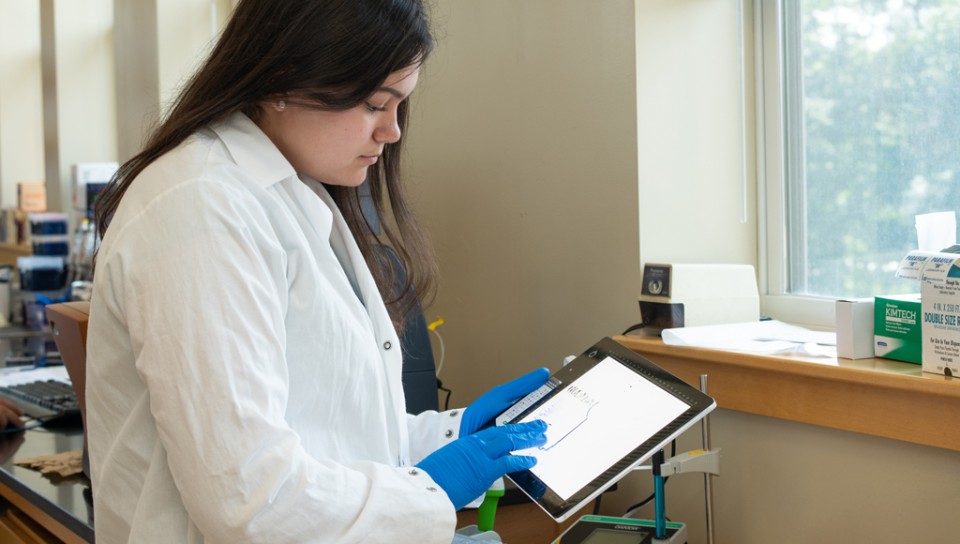 A student in a lab coat touches the graph on a tablet's screen